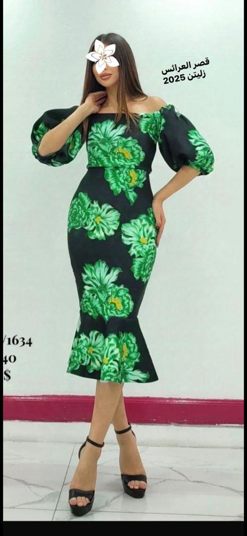 امرأة ترتدي طقماً أنيقاً مكوناً من بلوزة وسروال، تقف في متجر ملابس مع خلفية تعرض مجموعة متنوعة من الأزياء. النص الموجود في الصورة يقرأ قصر العرائس زليتن 2024، مما يضفي طابعاً عصريًا وثقة على المشهد.